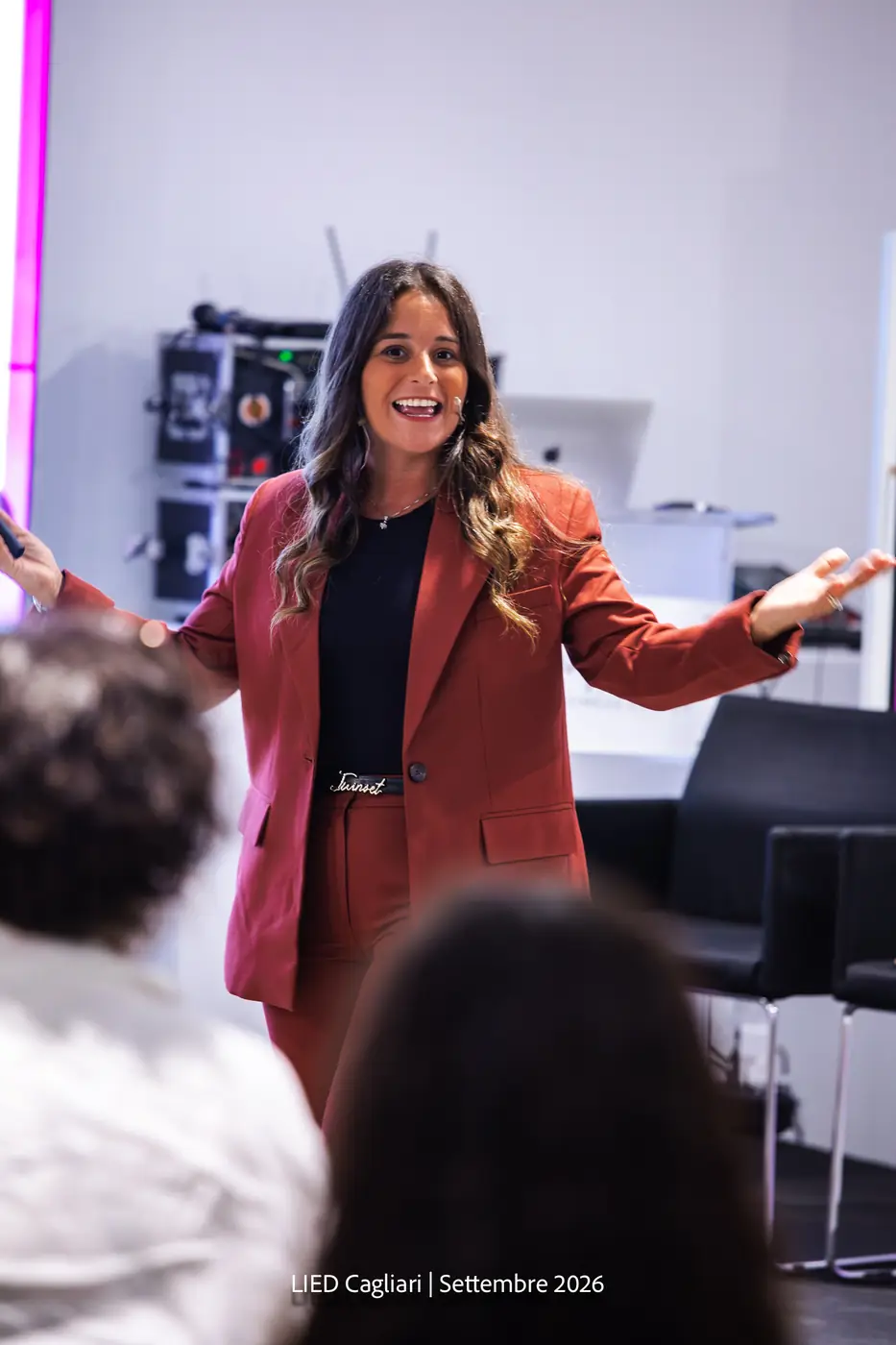 Cagliari — L'Impresa è Donna 2026 Una relatrice in completo mattone si rivolge alla platea con le braccia aperte
