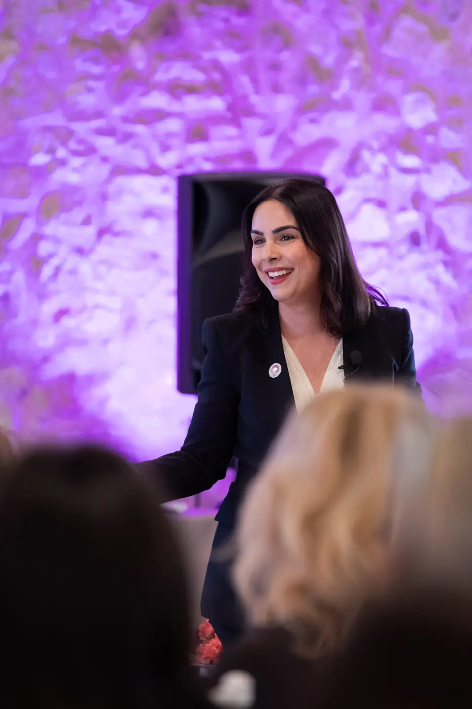 Desenzano del Garda — L'Impresa è Donna 2026 Una relatrice sorride mentre si rivolge alla platea, la parete in pietra illuminata di magenta