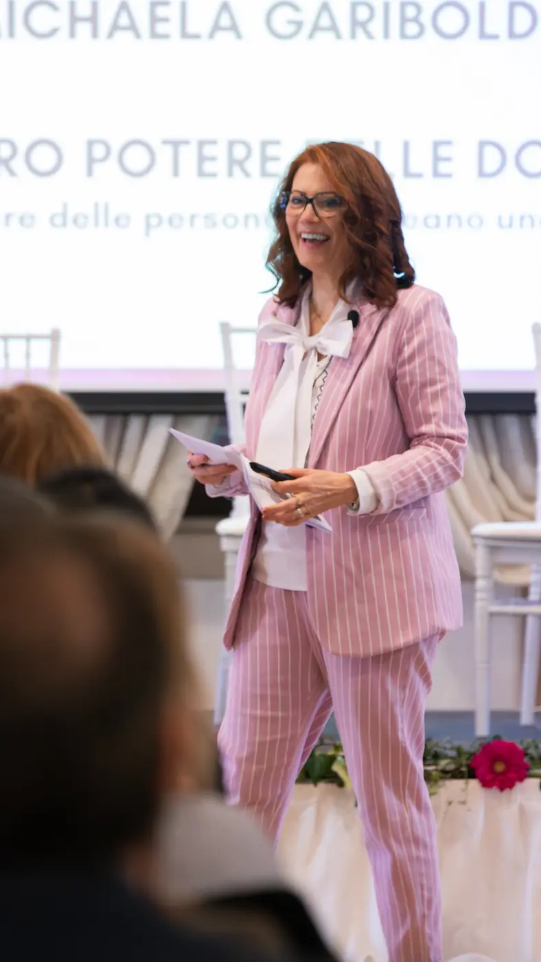 Desenzano del Garda — L'Impresa è Donna 2026 Una relatrice in tailleur rosa gessato presenta il suo intervento accanto allo schermo