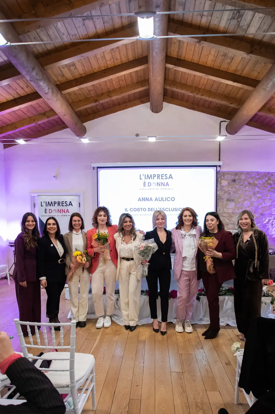 Desenzano del Garda — L'Impresa è Donna 2026 Il gruppo delle premiate sul palco di Desenzano, ripreso sotto le travi in legno