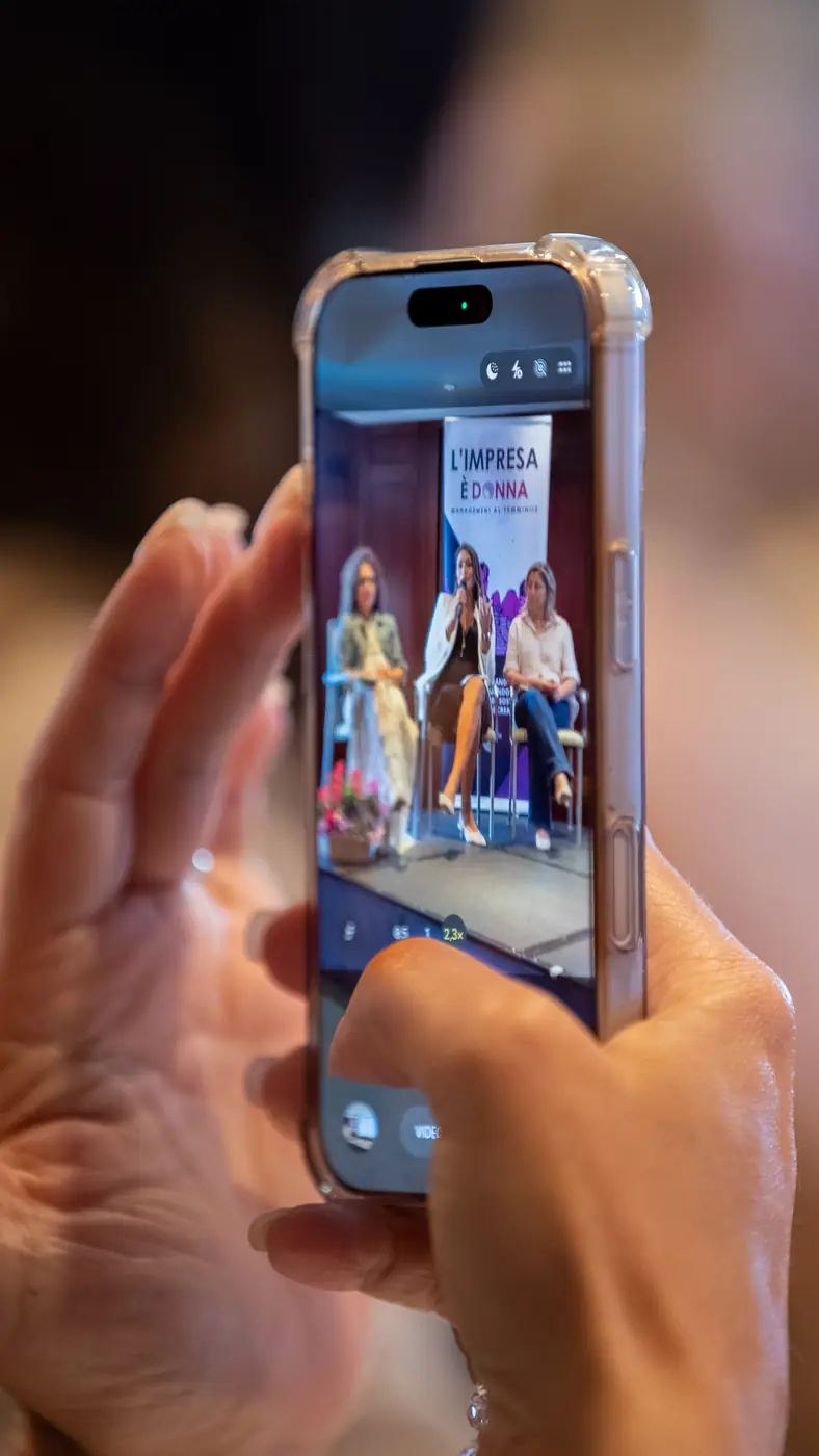 Genova — L'Impresa è Donna 2026 Uno smartphone inquadra la foto di gruppo finale della tappa di Genova