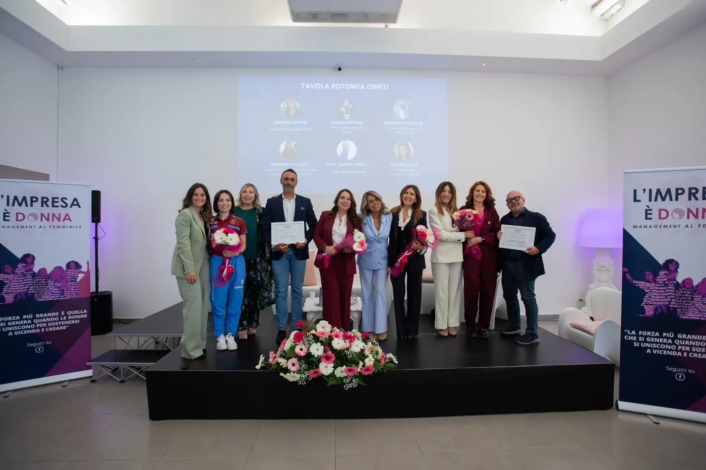 Palermo — L'Impresa è Donna 2026 Il gruppo delle premiate sul palco di Palermo tra i totem de L'Impresa è Donna